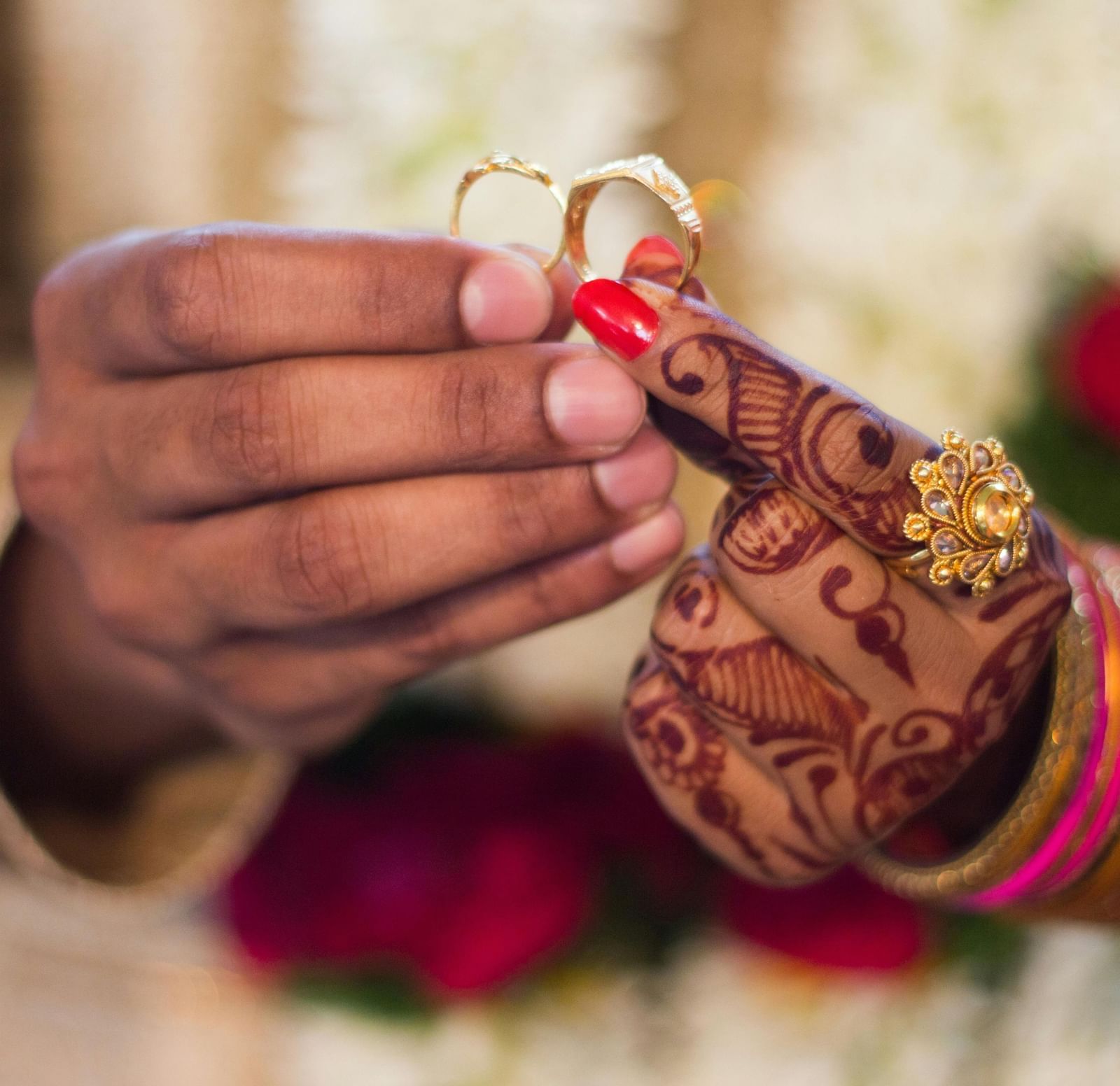 A close-up of a groom's hand giving a ring to a bride's hand during a traditional Indian wedding ceremony.