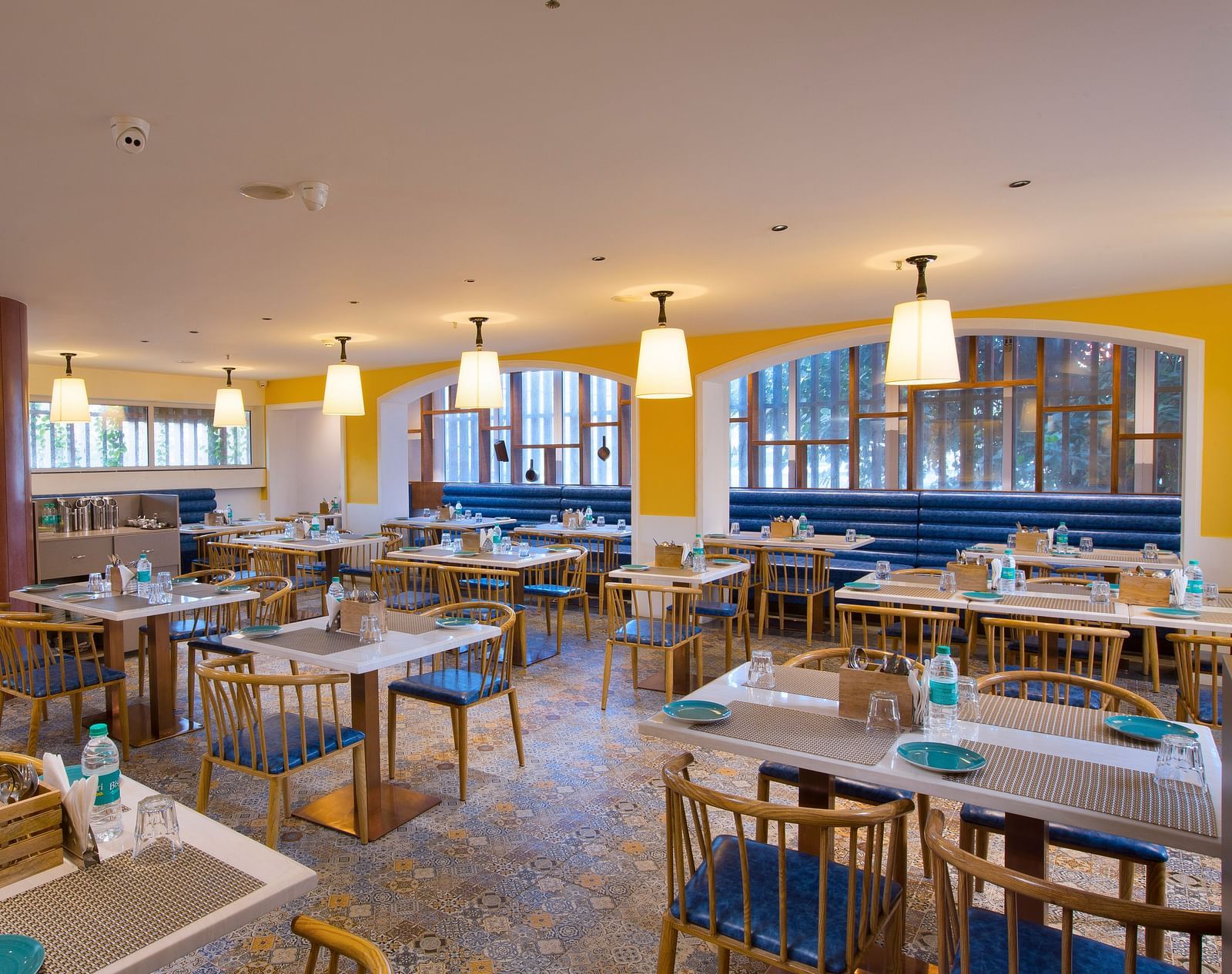 A bright and inviting restaurant interior with yellow walls, pendant lights and blue booth seating - Hotel Southend by TGI - Bommasandra, Bangalore