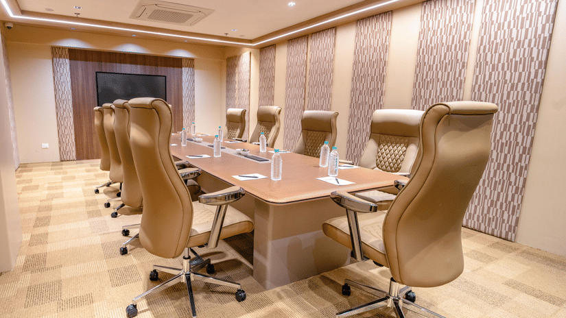 A well-lit boardroom featuring a long wooden table with multiple swivel chairs, a wall-mounted television, and patterned wall panels | Pride Elite Chhatrapati Sambhajinagar
