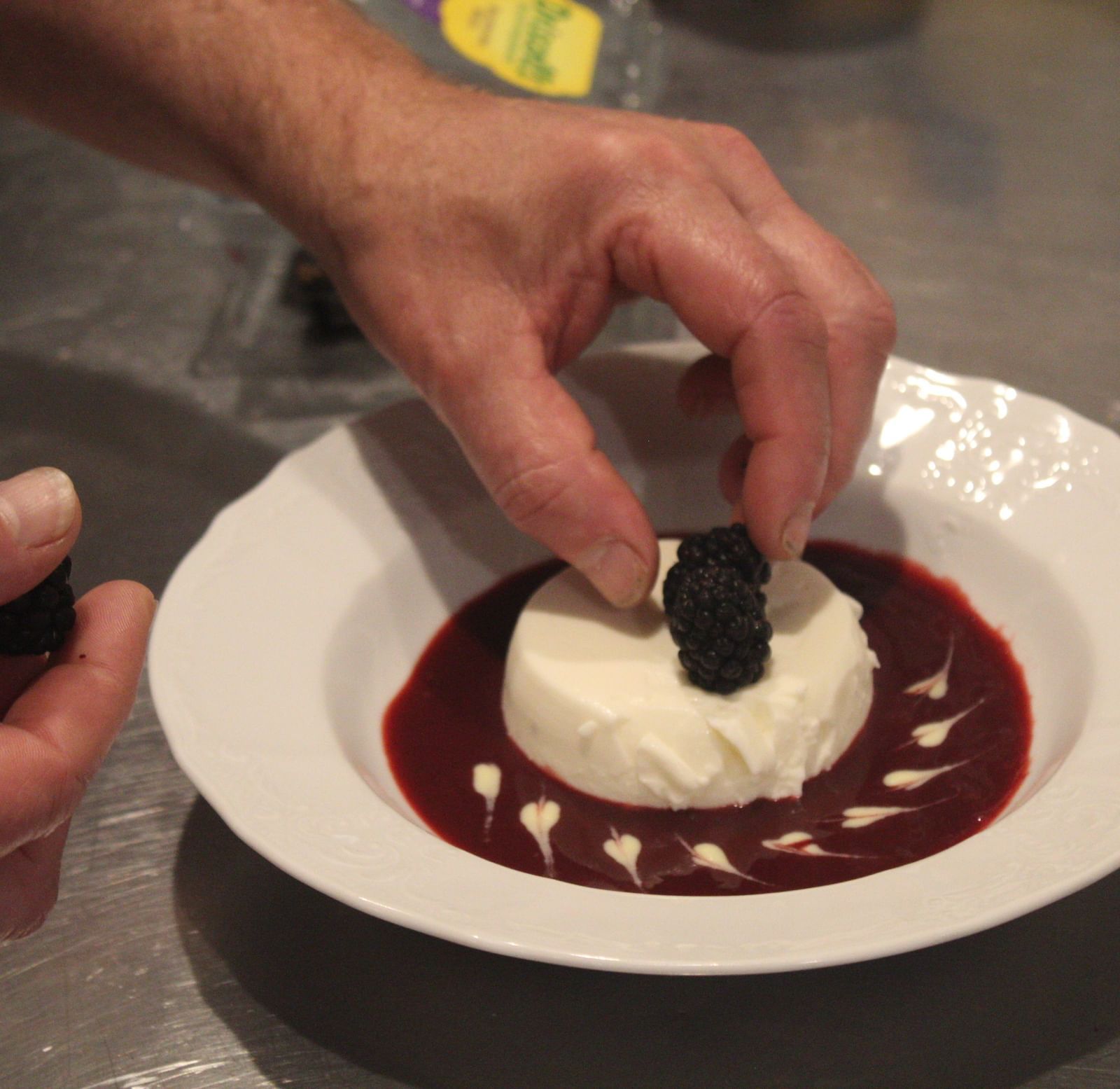 A hand placing garnish on a plated dessert with berry sauce.