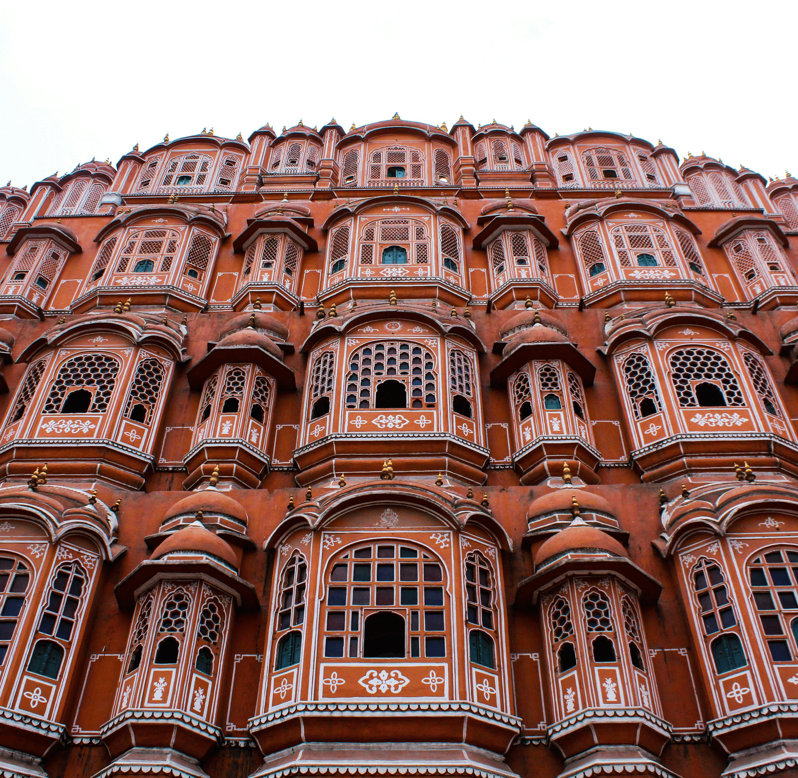 A low-angle view of the Hawa Mahal's 5-storey pink sandstone facade with its many ornate jharokha windows.