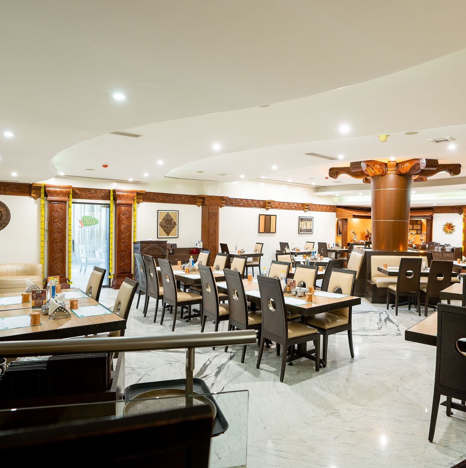 A spacious and well-lit restaurant interior with neatly arranged tables and chairs set for dining under a warm ambient lighting - The President Hotel Jayanagar, Bangalore