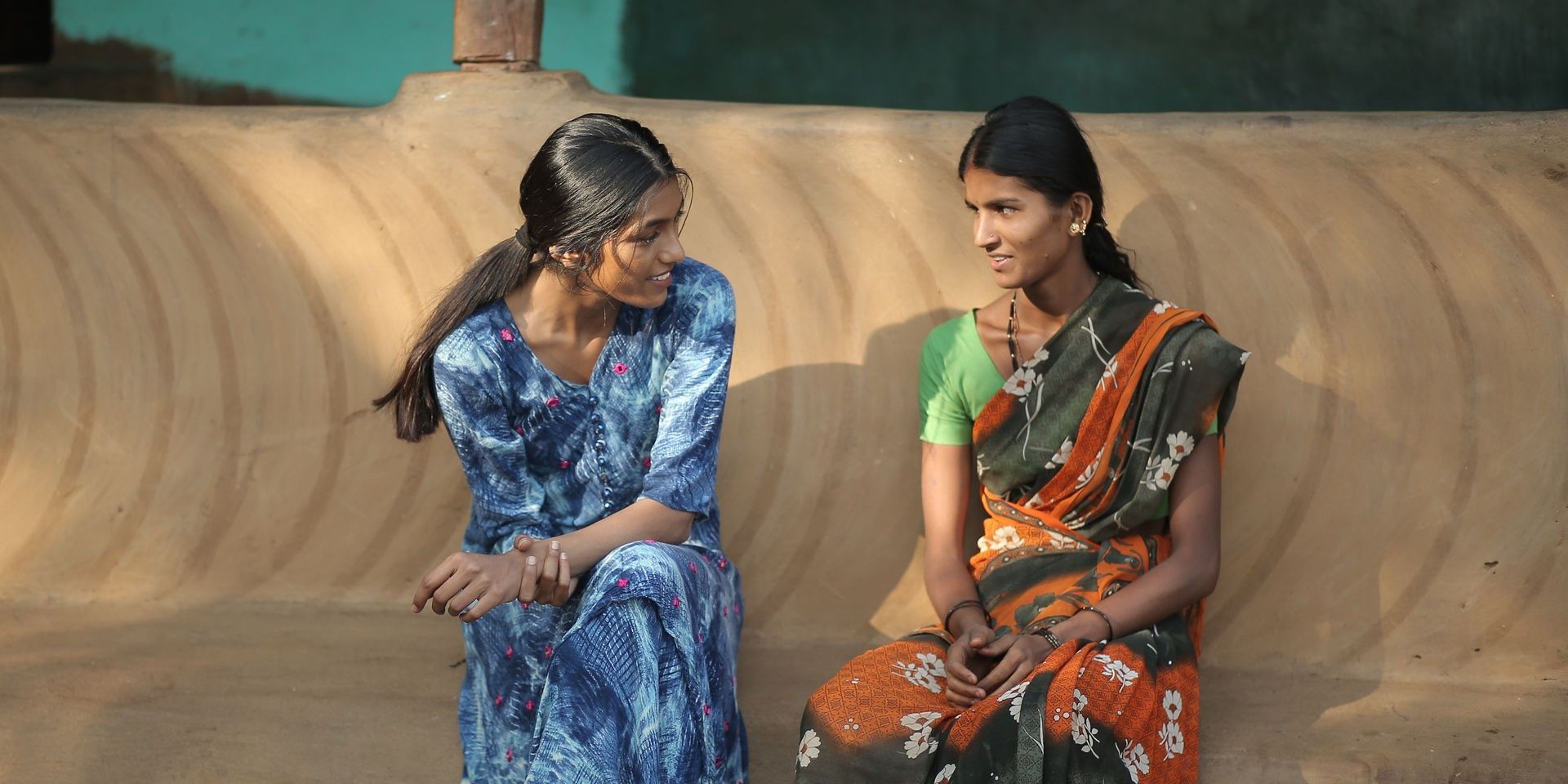 Two women in traditional Indian attire, rural setting.