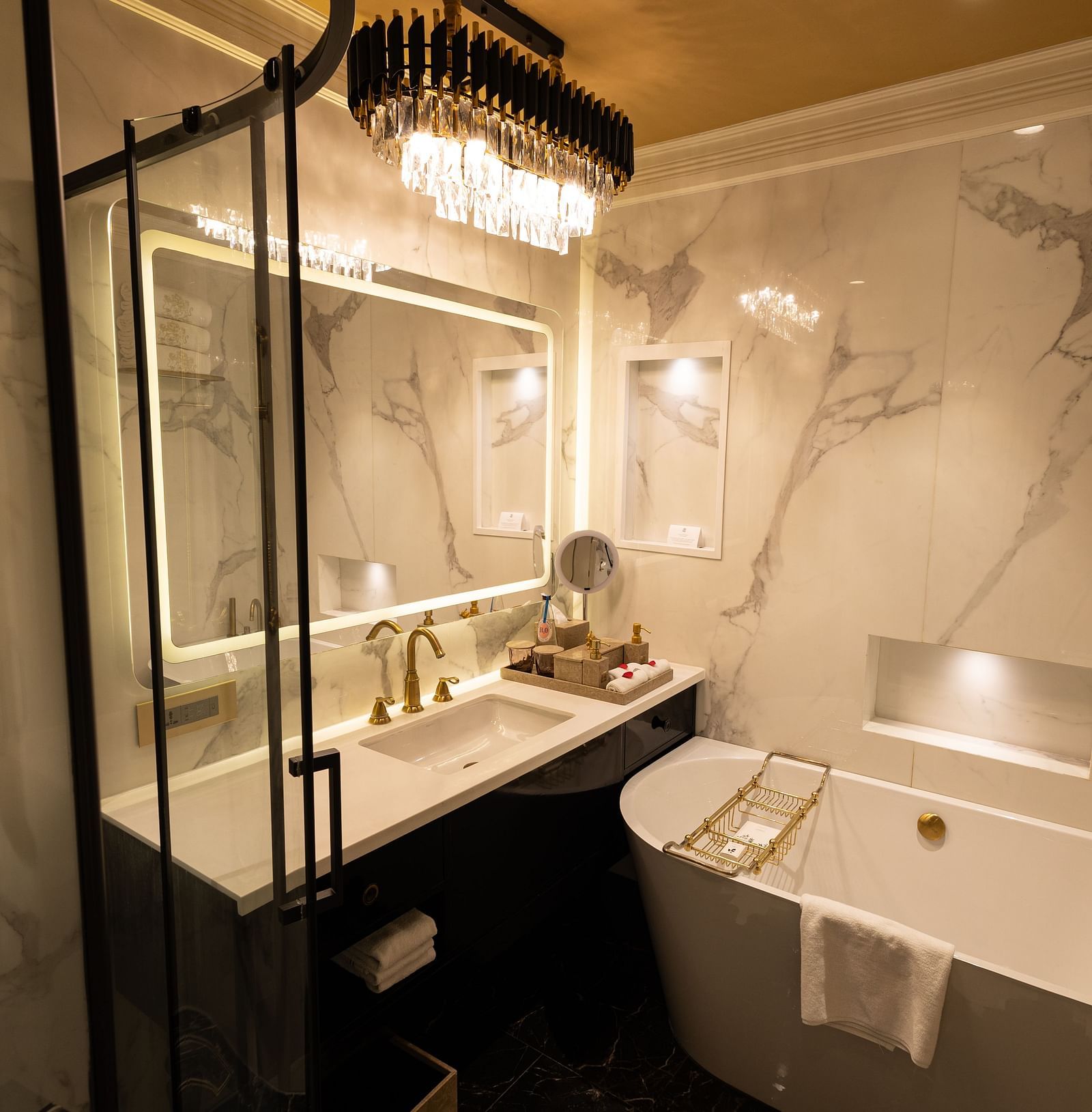 Washroom of the Executive Suite at The Claridges New Delhi, featuring a bathtub, wall-mounted mirror, and a chandelier hanging overhead