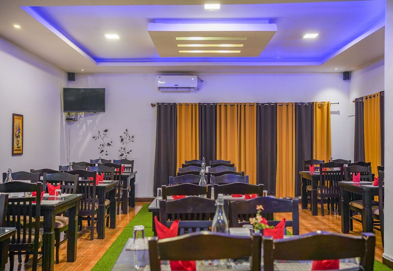 Image of a dining space with tables and chairs and a television mounted on the wall at Coorg Jungle Camp Backwater Resort, Kushalnagar.