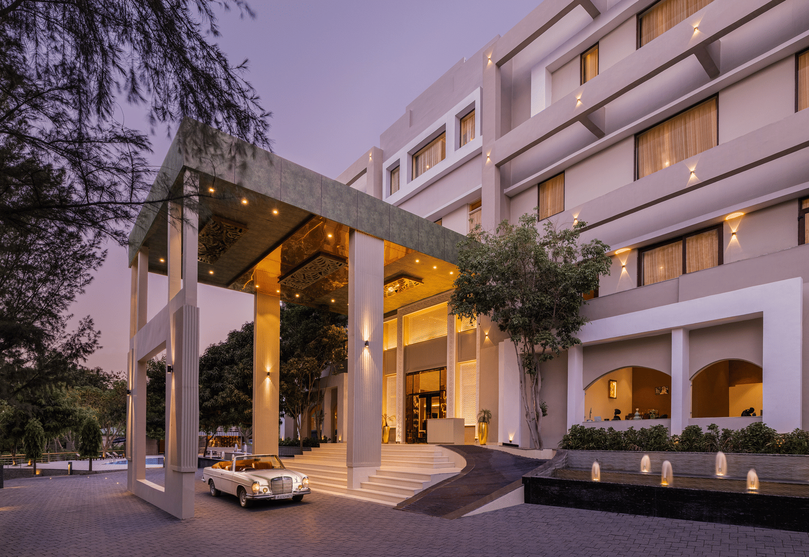 Facade of Essentia Luxury Resort & Spa, Udaipur with a prominent canopy with a car parked at dusk