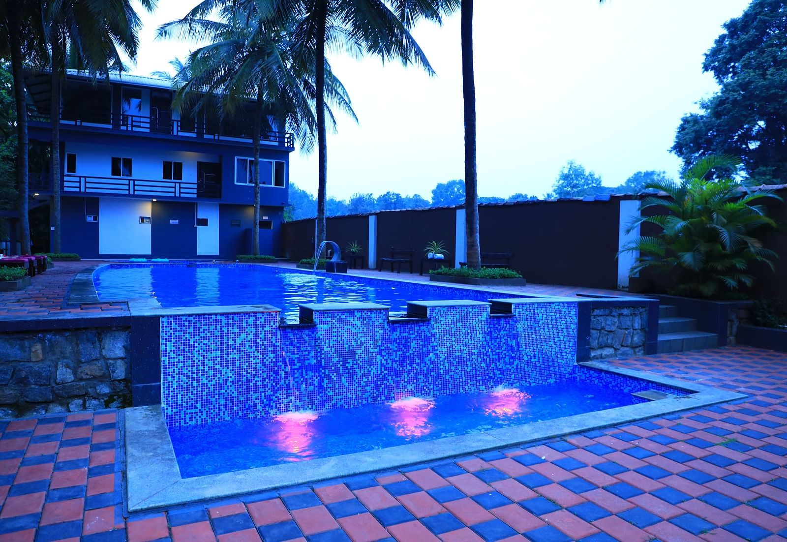 Image of a swimming pool with a building behind and trees beside at Parampara Resort & Spa, Kushalnagar.