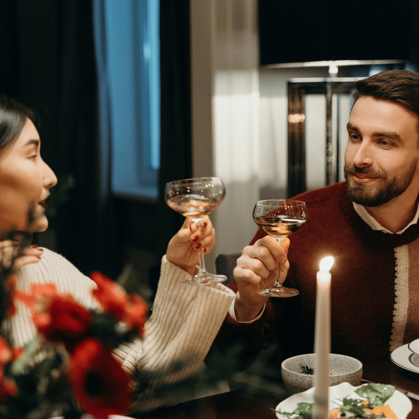 A couple looking at each other and holding their glasses up while being seated on a candlelight dinner