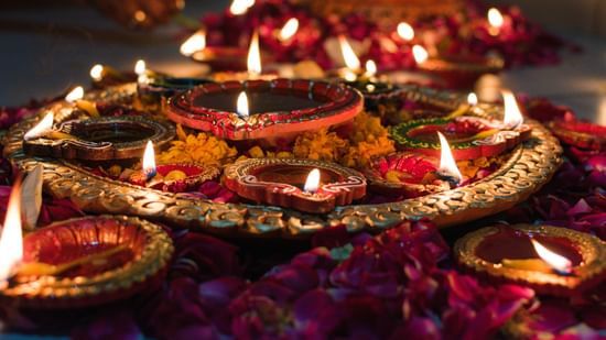 Arrangements of earthen lamps on a decorative tray over flower petals.