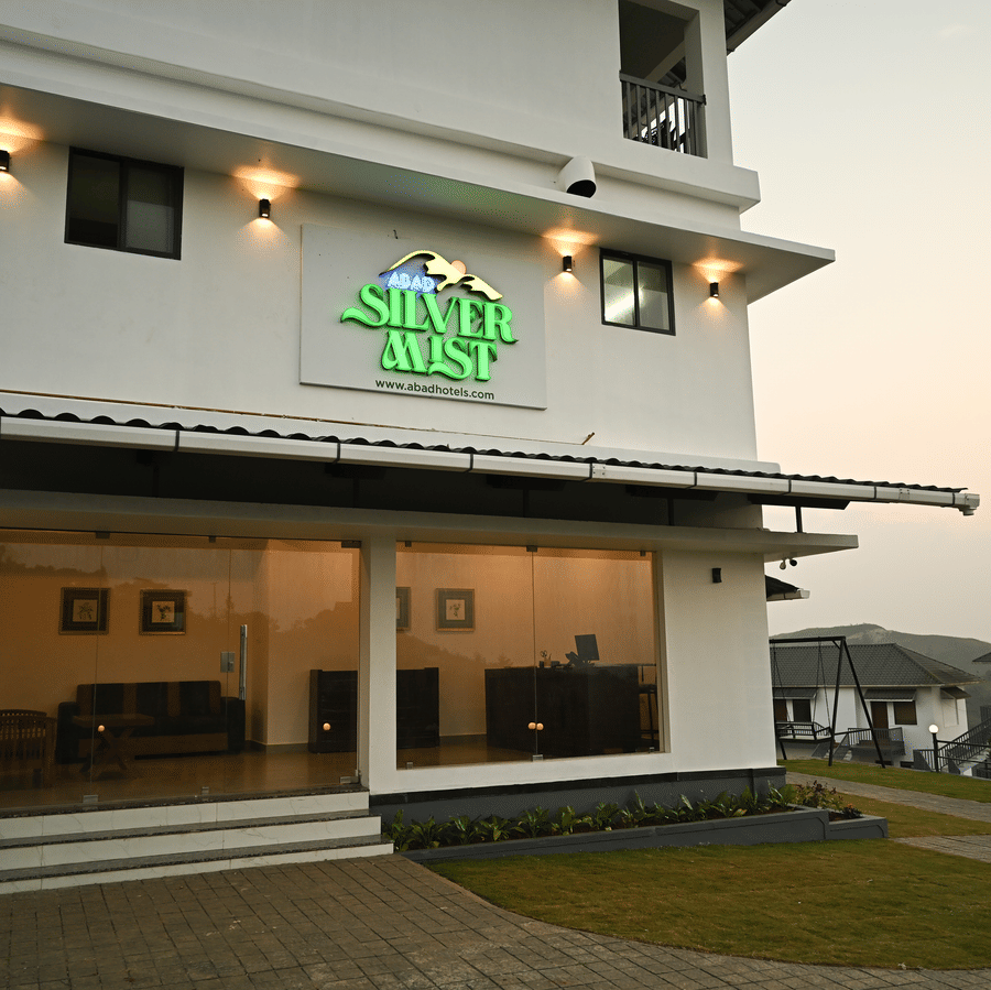 A white multi-storey building with a green resort sign above a glass-fronted entrance area at dusk | Abad Silvermist, Vagamon