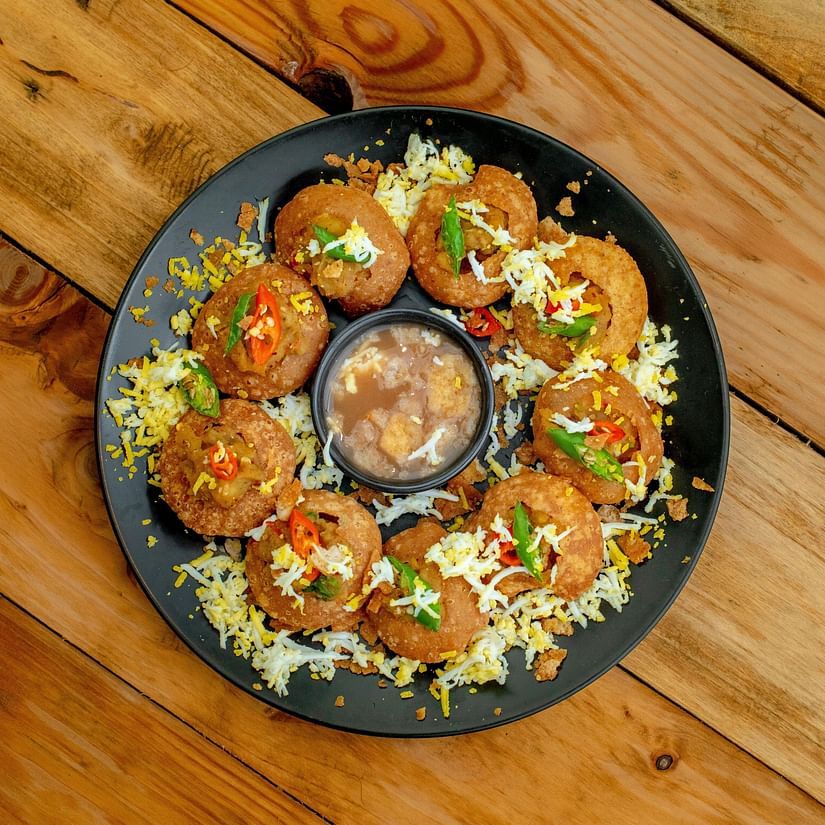 A plate of stuffed snacks garnished with herbs and spices, served with a side of sauce on a wooden table.