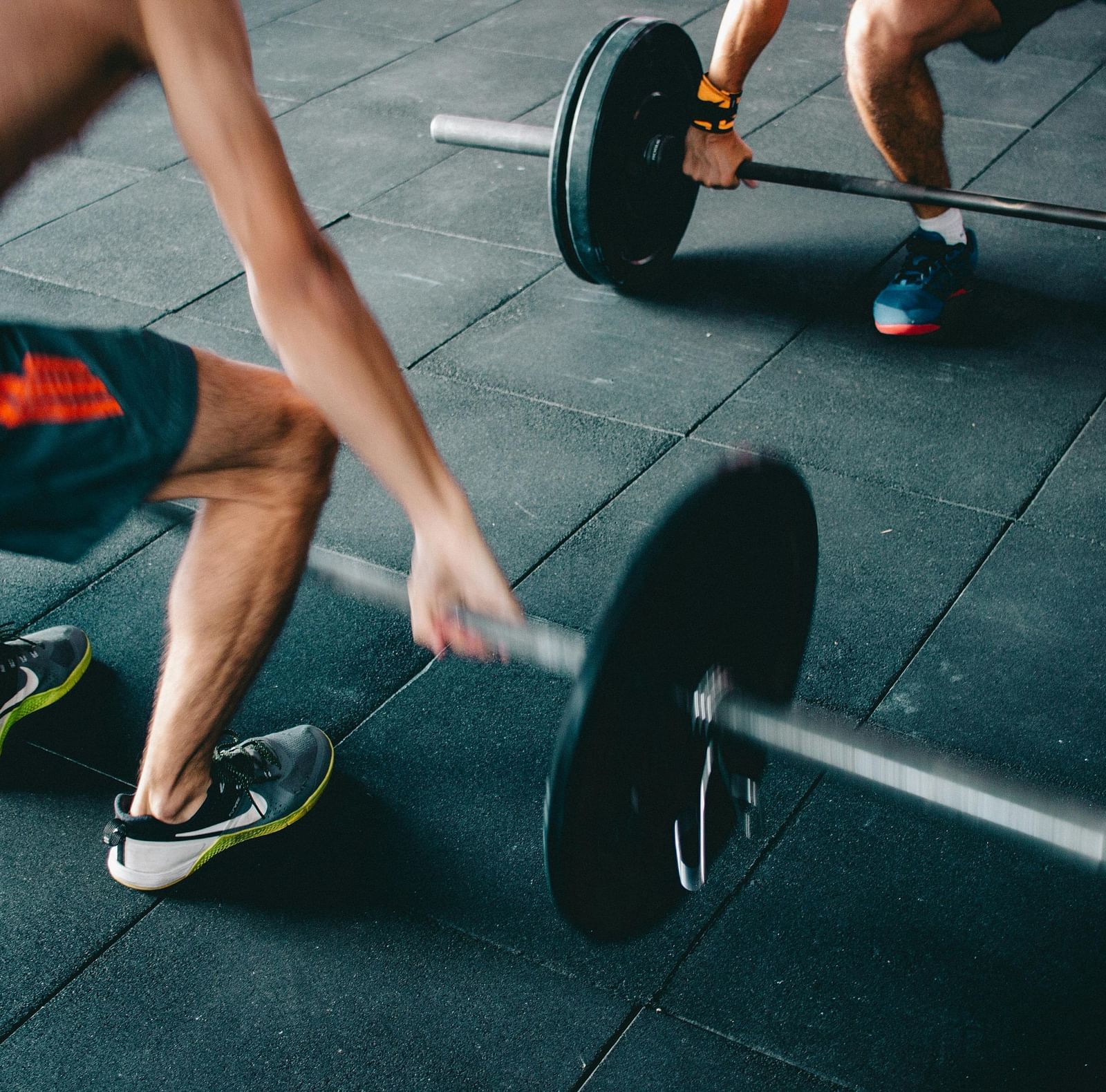 Two men are shown in a gym setting, lifting barbells with weights.