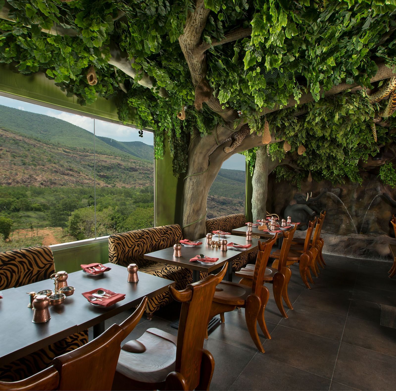 An image of a restaurant decorated with trees featuring several chairs and tables - The President Hotel, Hubli