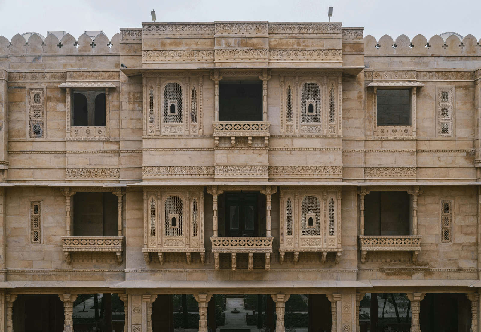 A detailed view of a light-coloured sandstone building facade with ornate balconies and carved stone latticework.