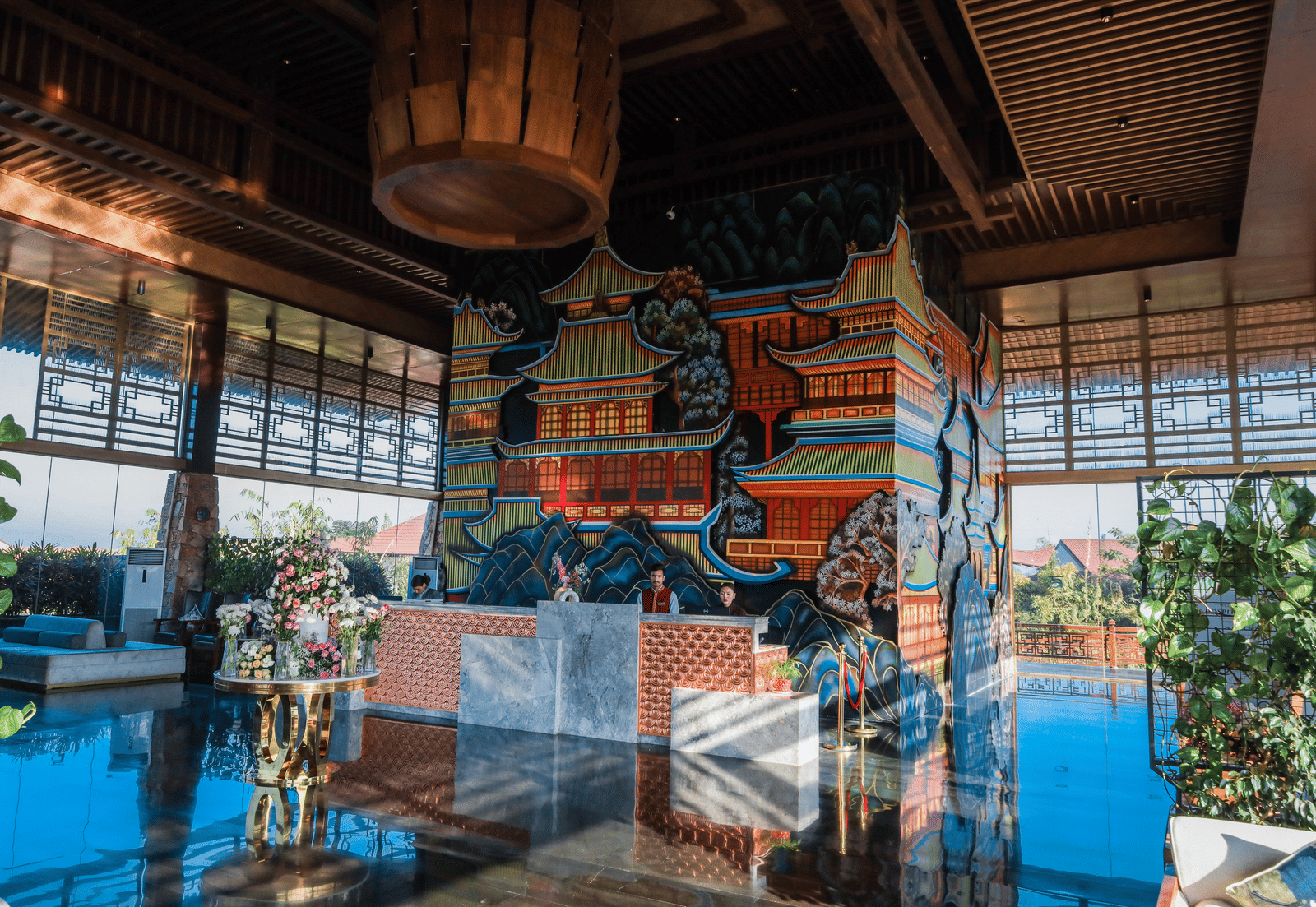 The brightly lit reception desk at Ananta Spa & Resort, Jaipur, stands in front of a colourful pagoda-themed mural and a large light.