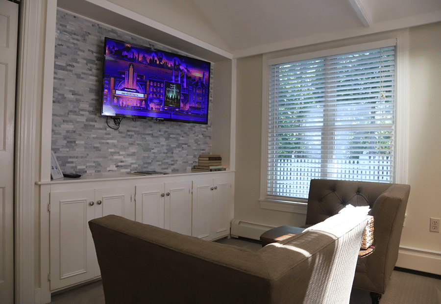 A cozy living room with a flat-screen TV, white cabinet, brown armchairs, and a window with blinds.