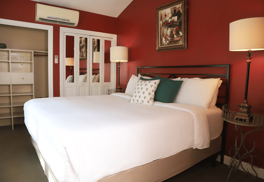 A wide-angle view of a guest room with a red accent wall, a large bed with white bedding, and a closet in the background.