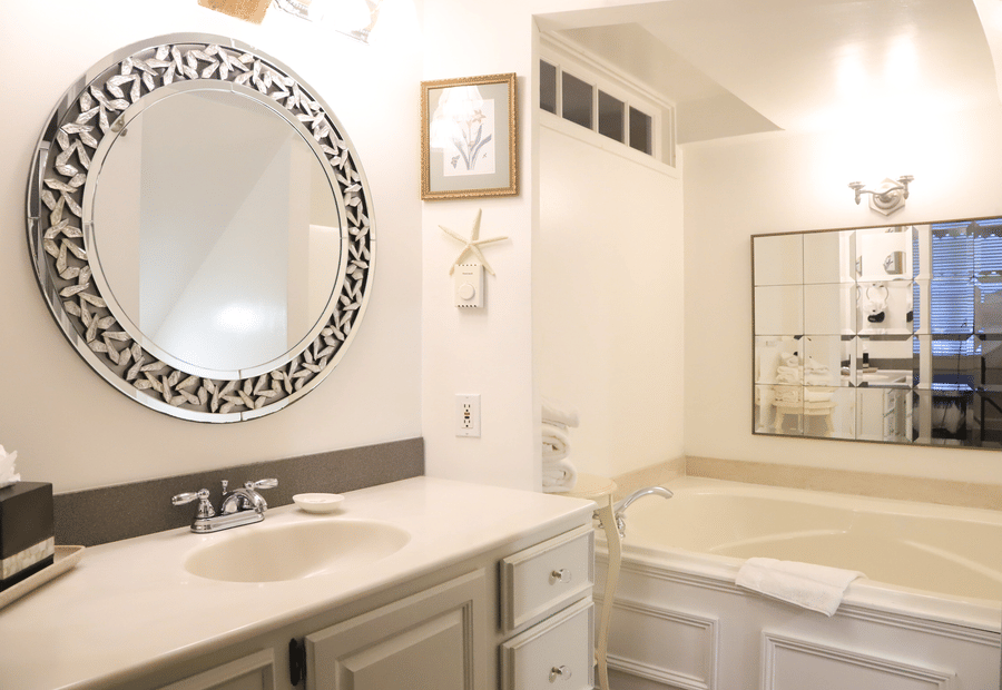 A clean and well-lit bathroom with a round mirror, white sink, and tub