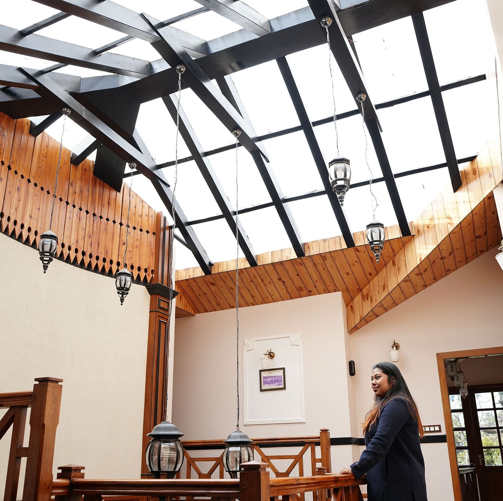 A woman stands in a bright, modern interior space with a high glass ceiling and wooden accents at Orisno Hotel  & Spa.
