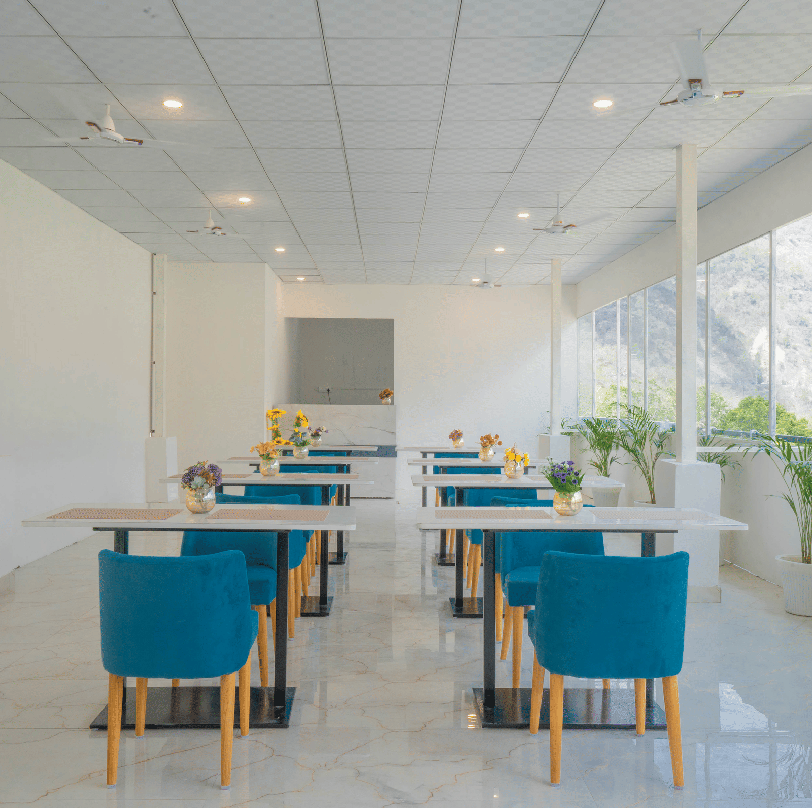 A spacious dining hall at Perfectstayz Value Alpine Retreat, Rishikesh with white interiors and neatly arranged chairs and tables.