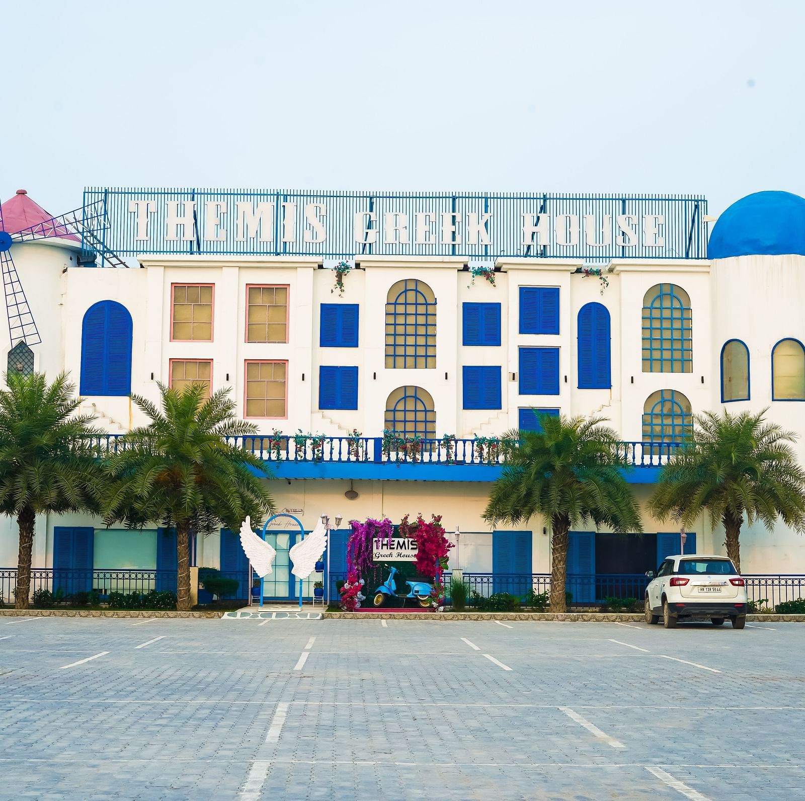 A facade image of Themis Greek House with a parking lot in the front yard 