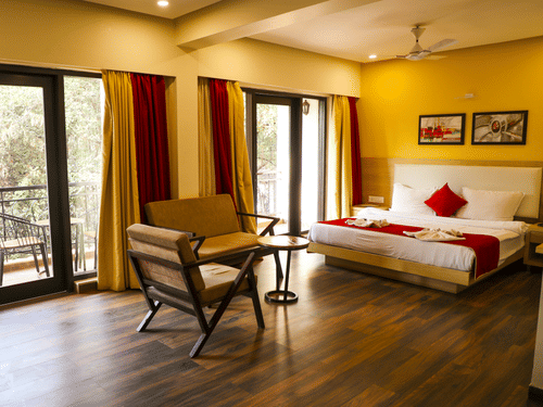 An overview of the Executive Suite with a double bed, chairs and balcony in view - Rosetum Anjuna.