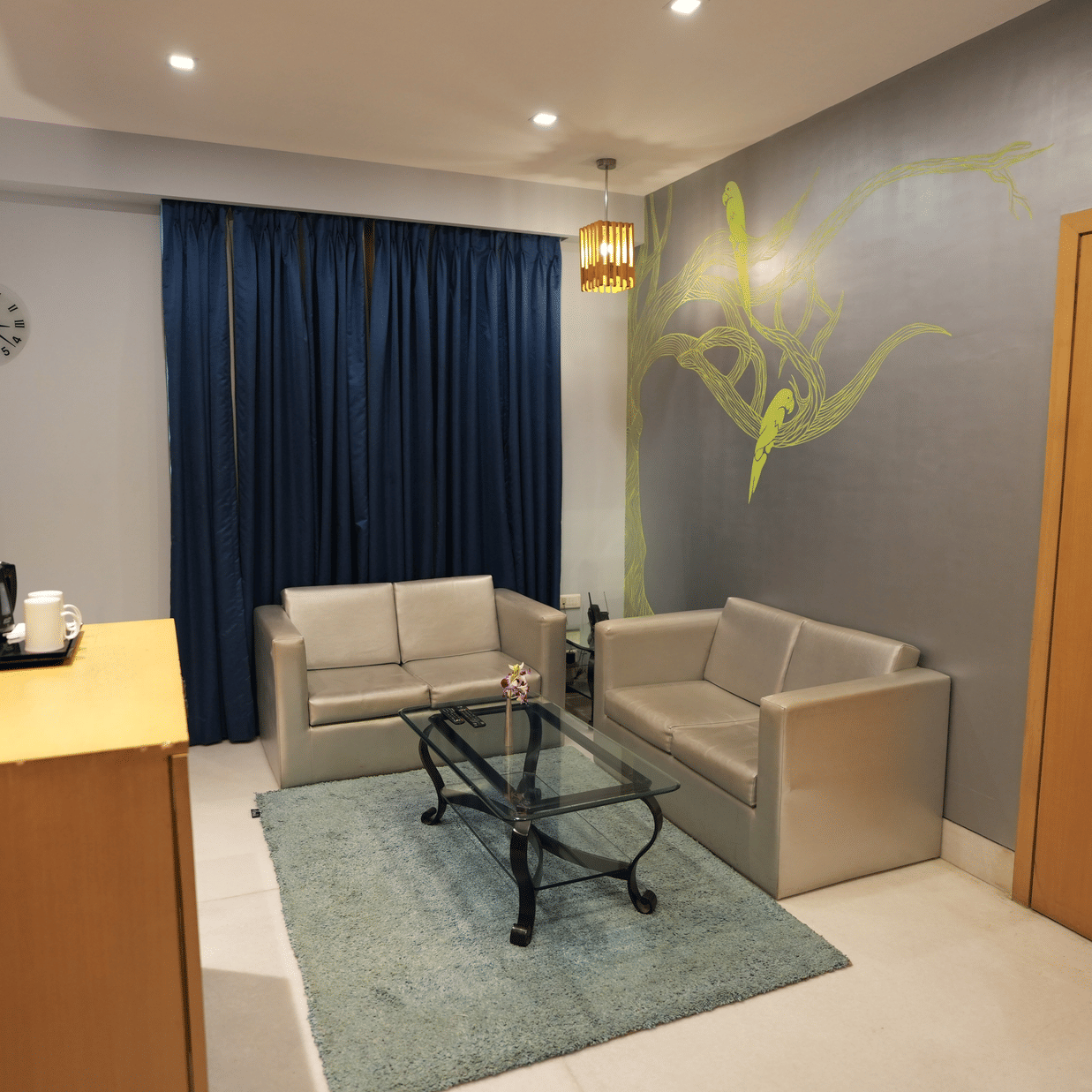 A room at The Beatle Hotel, Powai with two couches, carpet, a glass table and cupboard. 