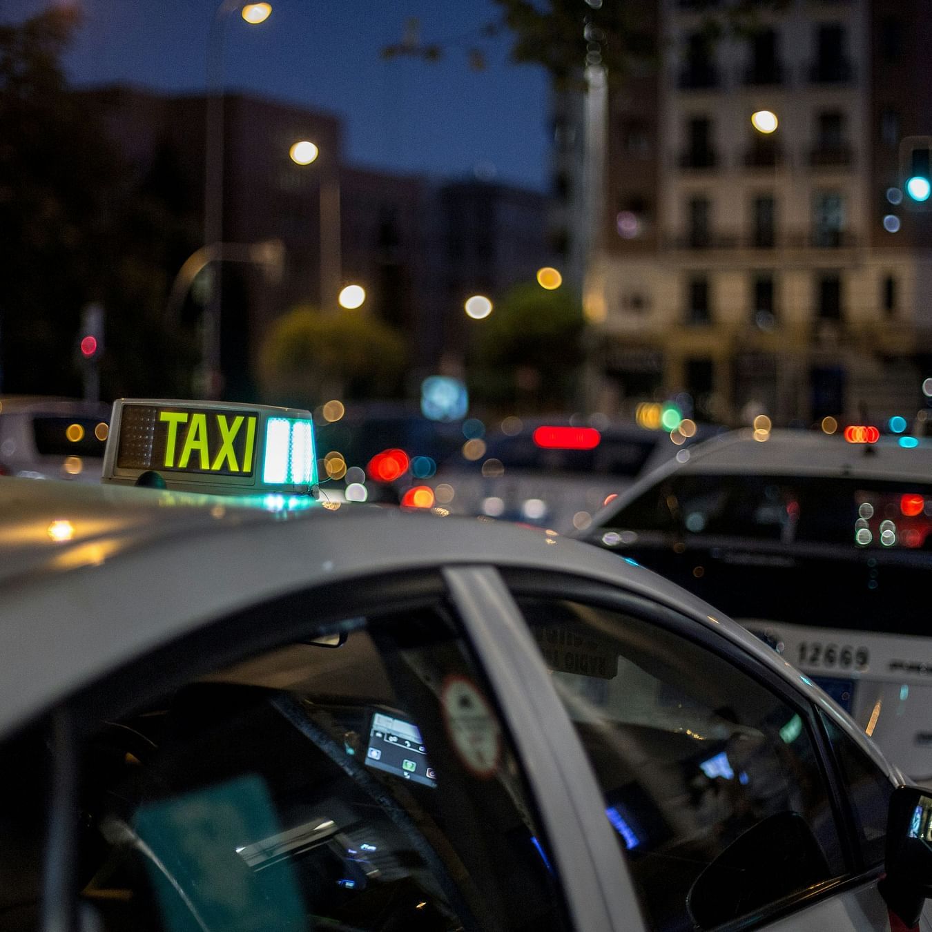 Illuminated taxi sign on top of a car in a bustling city street at dusk