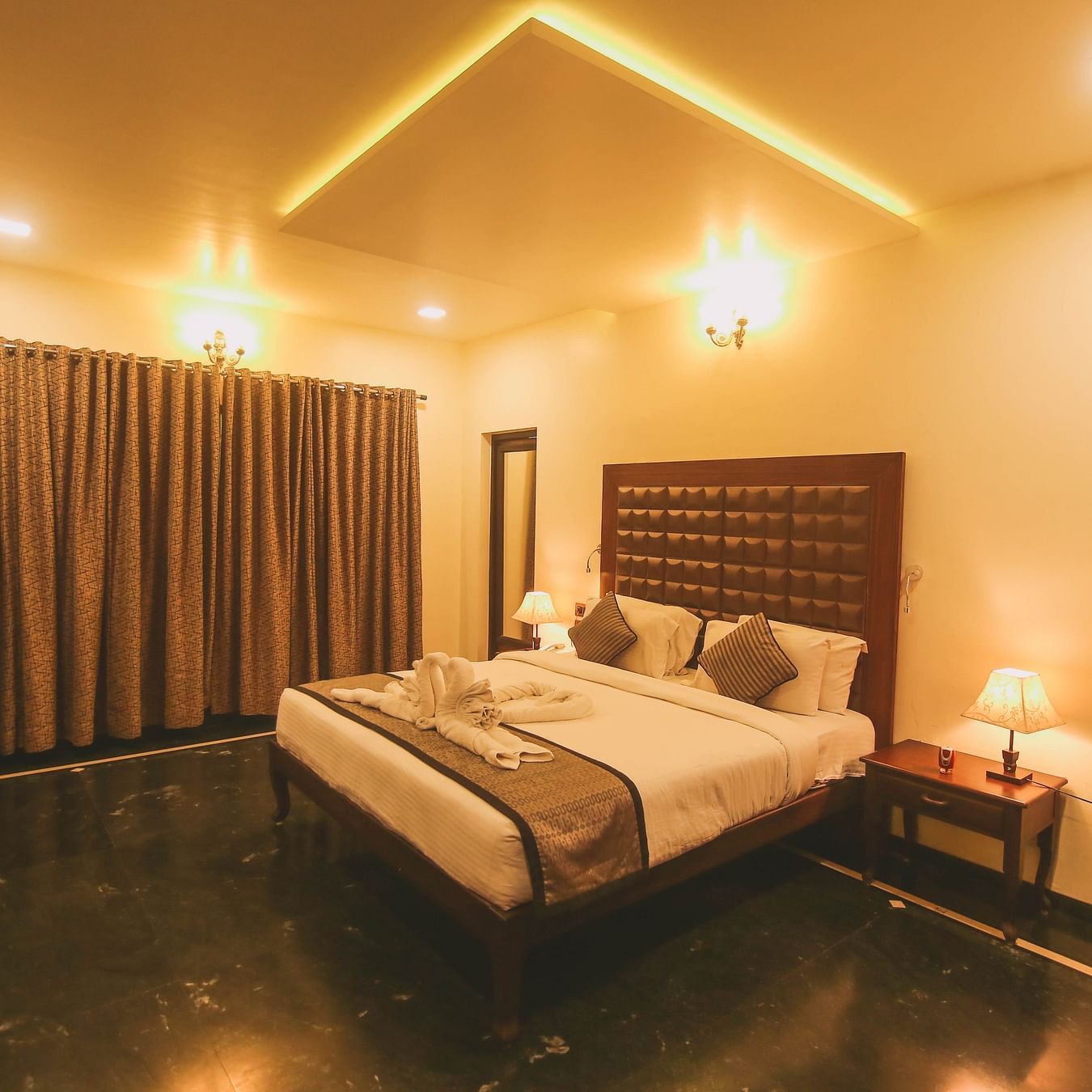 A king size bed in a warmly lit room with a lamp placed on the nightstand next to it at Damanganga Valley Resorts