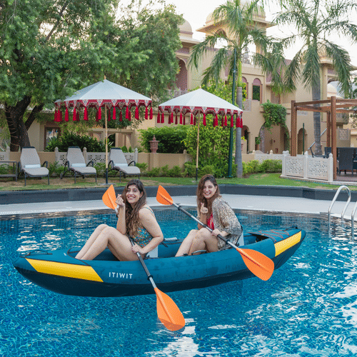 two women sitting in a kayak holding the oars that is kept in the swimming pool - Heritage Village Resorts & Spa, Manesar