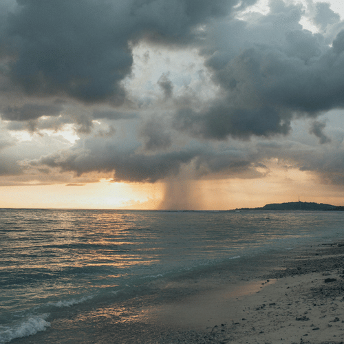 Rain falling over the ocean with the sun setting on the horizon, creating a moody scene.