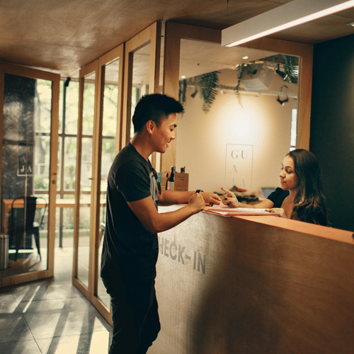 A young man checking in at a hostel reception desk with a female attendant
