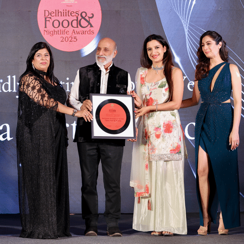 Four people on stage holding a framed award for 'Pet-Friendly Destination of the Year 2025' given to Tijara Fort & Palace at the Delhiites Food & Nightlife Awards.