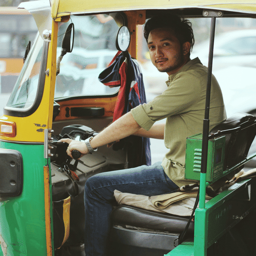 A close up of an auto driver sitting in his auto rickshaw and posing for a picture.