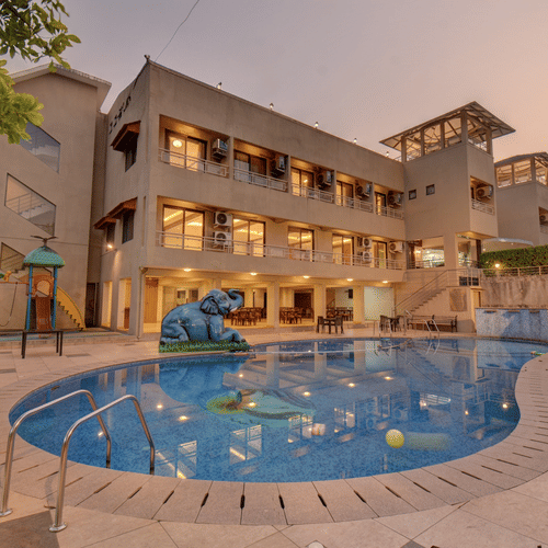 Evening view of the VITS Lonavala in the background and the pool in the foreground covered by trees on either side, ideal for a destination wedding in Lonavala