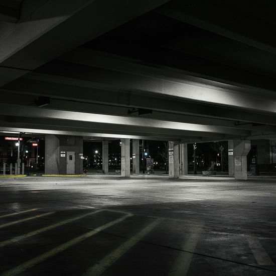 A dimly lit, stark interior space with strong shadows, possibly an underground car park or tunnel.