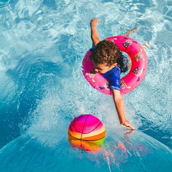 A kid wearing blue t-shirt on a pink inflatable pool tube in the pool
