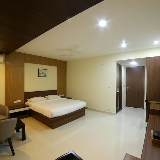 A room featuring a well made bed sofa chairs a TV and a wall painting - Mysore Gate Hotel Bangalore