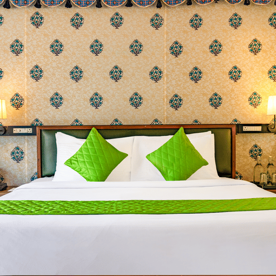 Nature Trails Kudalika premium AC tent double bed closeup with green quilted pillows, white bedding, green bedrunner, block-print headboard wall and brass wall lamps.