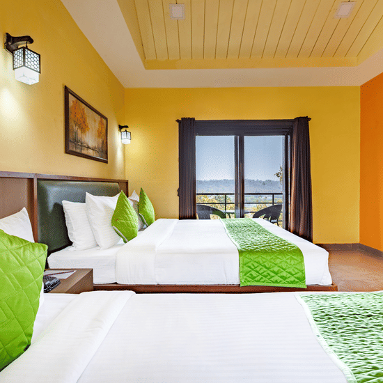 Nature Trails Kudalika river view room with two beds, green bedding, yellow and orange walls, wall lights, framed painting and open balcony with river and hill view.