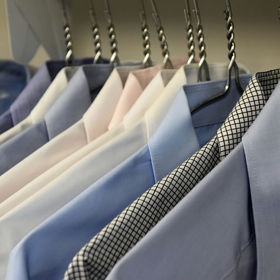 Neatly arranged dress shirts hanging in a wardrobe with patterned ties draped over hangers.