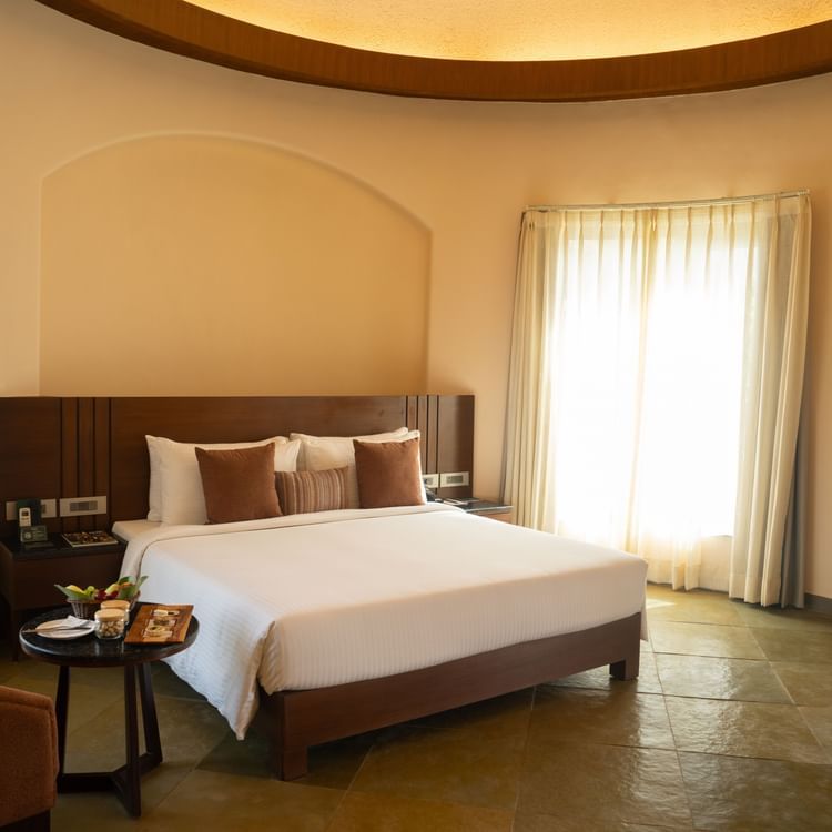 A warm bedroom with a double bed, soft lighting, and full-length mirror near the window at Ananta Spa and Resort, Ajabgarh.