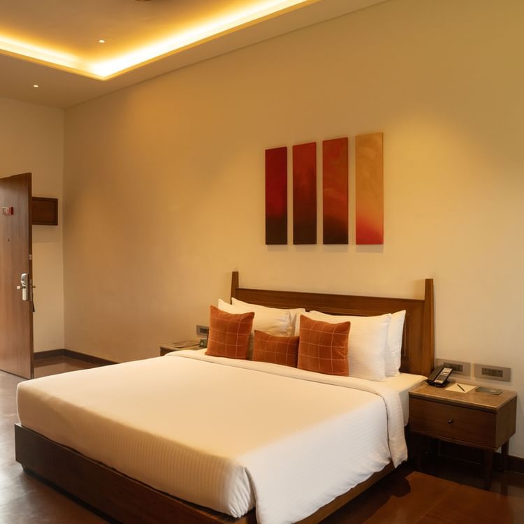 Cosy bedroom with warm lighting, modern artwork, bedside table, a seating area, and outdoor access at Ananta Spa and Resort, Ajabgarh.