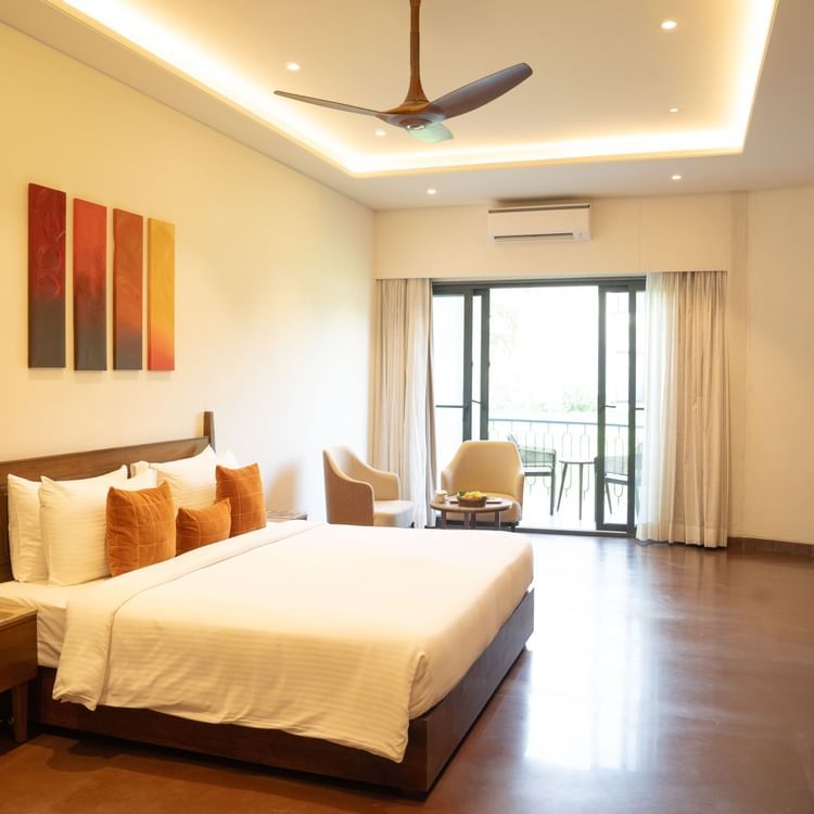 Spacious bedroom with wooden flooring, modern decor, and large glass doors opening to a sit-out at Ananta Spa and Resort, Ajabgarh.