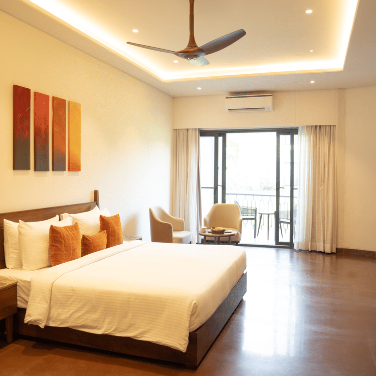 Spacious bedroom with wooden flooring, modern decor, and large glass doors opening to a sit-out at Ananta Spa and Resort, Ajabgarh.