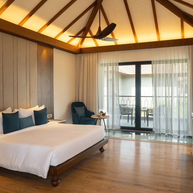 A spacious modern bedroom with a king-size bed, wooden flooring, and a balcony with glass doors at Ananta Spa and Resort, Ajabgarh.