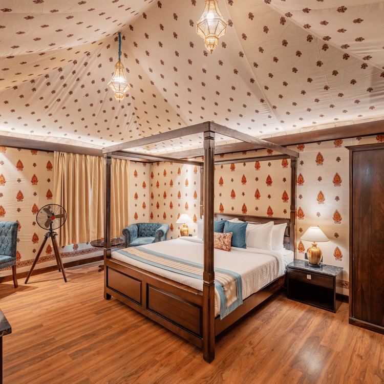 Elegant bedroom with four-poster bed, patterned wallpaper, wooden flooring, wardrobe, blue chairs, and telescope by window.