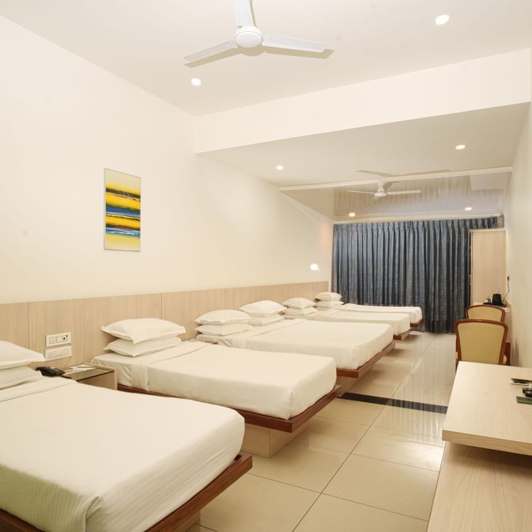 Hotel room interior featuring multiple single beds lined up, a wall-mounted TV, and an air conditioning unit at Arawali Ananta Elite, Jaipur.