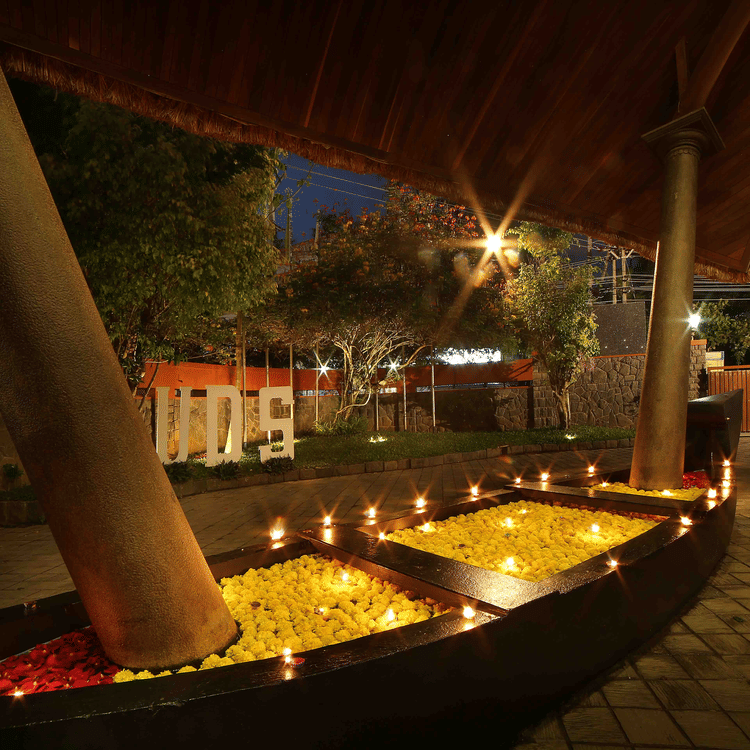 A decorative boat filled with yellow and red flower petals and candles illuminates the outdoor area of Uday Samudra Leisure Beach Hotel at night