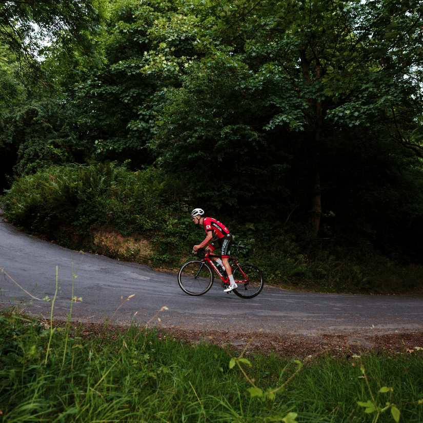 A person is cycling on a path in a green forest.